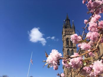 Low angle view of cherry blossoms against sky with flag at half-mast and university tower