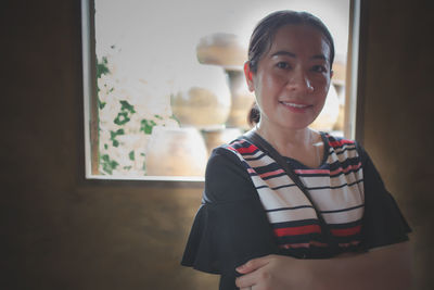 Portrait of a smiling young woman standing against window