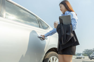 Woman holding mobile phone while standing on car