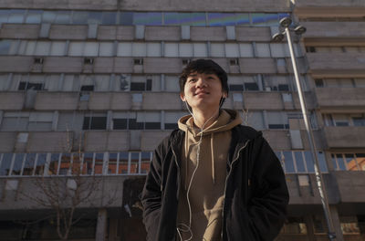 Asian teenage boy with earphones against building on street. madrid. spain