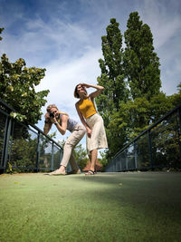 Low angle view of beautiful woman photographing while female friend looking away at park