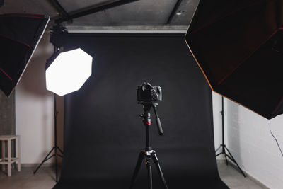 Interior of modern photo studio with octaboxes and professional photo camera on tripod against black background
