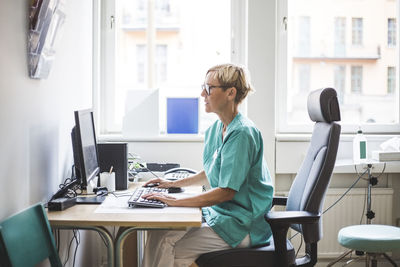 Side view of mature female doctor working over computer while sitting in clinic