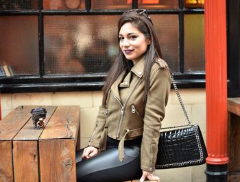 Portrait of beautiful woman wearing jacket by table at cafe