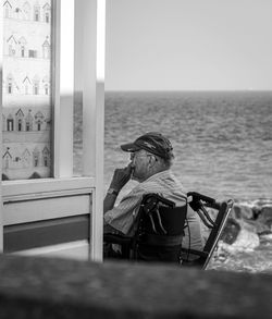 Woman sitting on chair by sea against sky