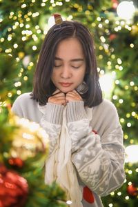 Portrait of smiling young woman standing by christmas tree