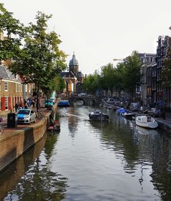 Boats moored in canal amidst buildings in city against sky