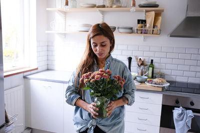 Woman carrying flower vase while standing at kitchen