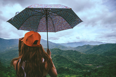 Rear view of woman holding umbrella against mountains