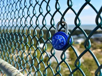 Blue padlock hanging from chainlink fence