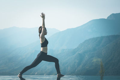 Side view of woman exercising on infinity pool against mountains