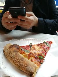 Midsection of man using mobile phone with pizza on table