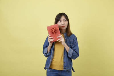 Portrait of young woman standing against yellow background
