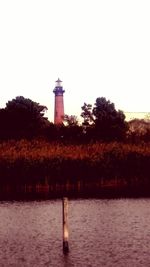 Lighthouse by trees against clear sky