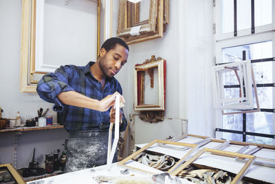 Confident young male craftsperson rubbing sand paper on frame at workshop