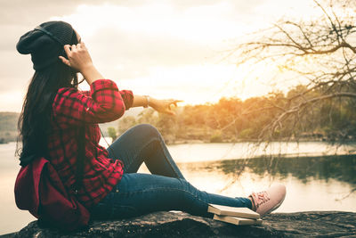 Woman sitting by lake against sky