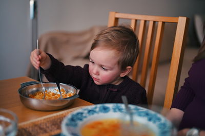 Little toddler sitting at the table and eating soup