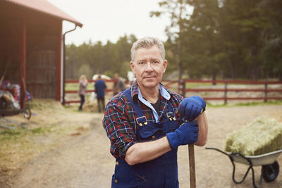 Portrait of confident farmer holding pitchfork while standing in farm