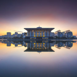 Buildings by lake at sunset