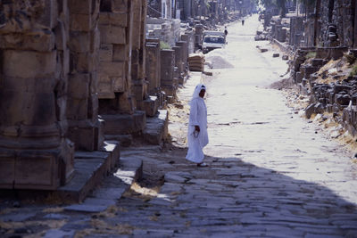 Rear view of woman walking on footpath amidst buildings