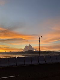 Road by silhouette mountain against orange sky