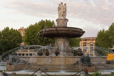 Statue by fountain against sky in city