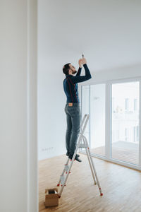 Home owner standing on ladder fixing light installation