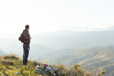 Rear view of man standing on mountain against sky