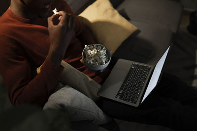 Man watching movie on laptop eating popcorn at home