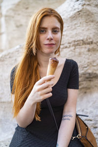 Young ginger woman with half eaten ice cream cone sitting in city