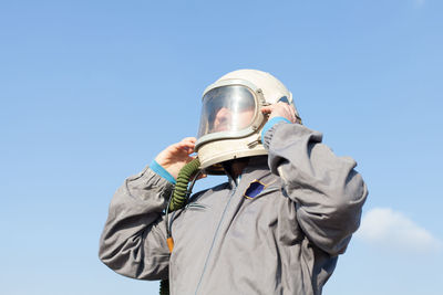 Low angle view of man wearing helmet against blue sky