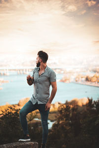 Young man standing in sea against sky during sunset