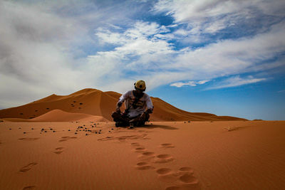 Man on sand dune in desert against sky