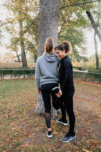 Full length of women exercising by tree trunk during autumn