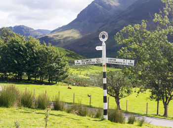 Road sign by trees on mountain against sky