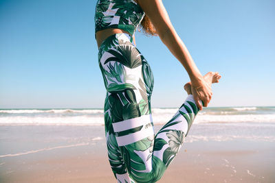 Low section of woman jumping on beach against clear sky