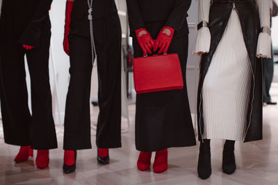 Fashion details of a knitted warm white dress, red leather gloves, handbag and black outfits