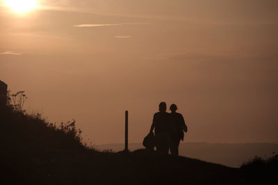 Rear view of silhouette men on land against sky during sunset