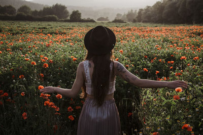 Rear view of woman standing by flowering plants on field