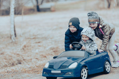 Three happy children playing with big old toy car in countryside, outdoors.