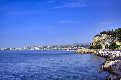 Sea by buildings against blue sky