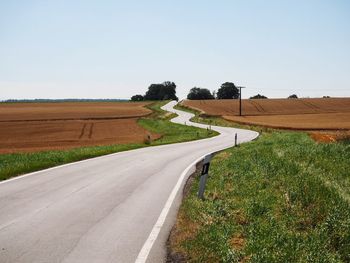 Empty road amidst field against clear sky
