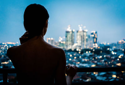 Rear view of shirtless woman looking at cityscape against sky