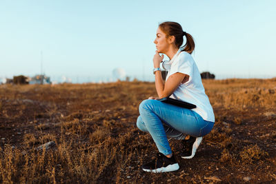 Side view of young woman sitting on land