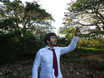 Happy young man standing by tree against plants