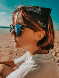 Portrait of young woman wearing sunglasses while sitting at beach