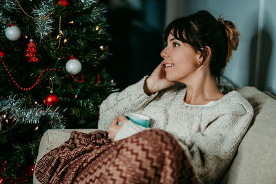 Portrait of young woman standing by christmas tree at home