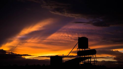 Silhouette solar water heater against cloudy sky during sunset