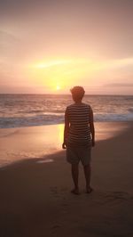 Rear view of woman standing on beach during sunset