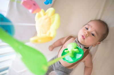 High angle view of shirtless baby boy with toys lying in crib